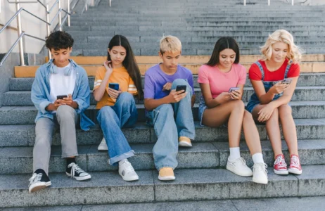 A group of individuals sit together on outdoor steps, each using a smartphone during their free time.