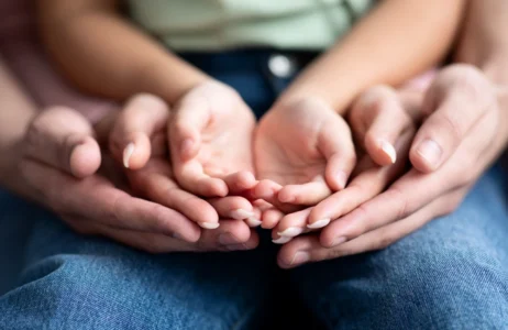 Multiple hands rest gently together in a layered hold, symbolizing support and connection.