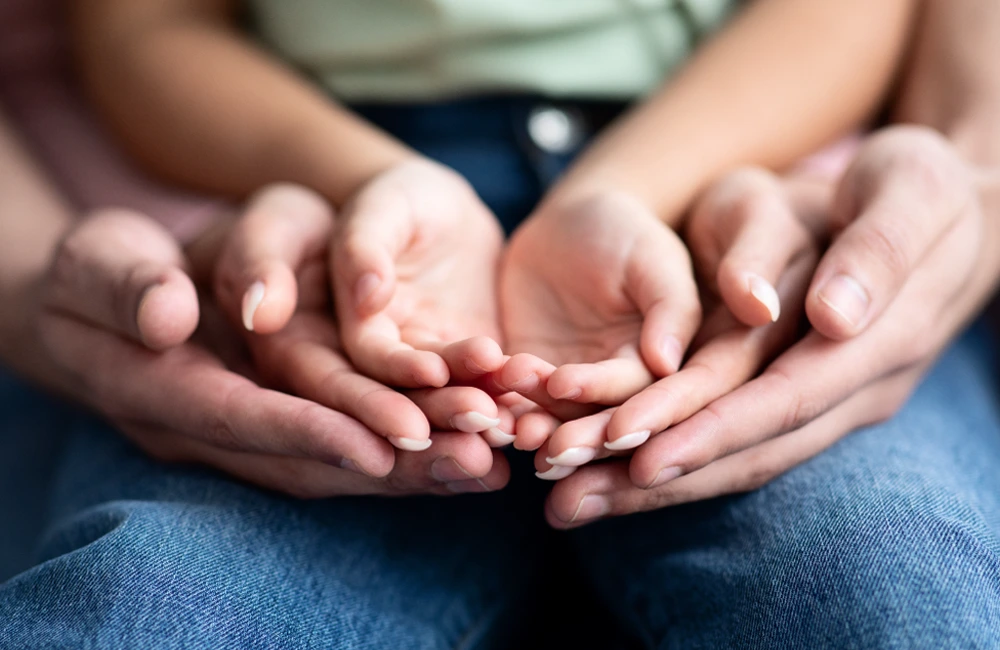 Multiple hands rest gently together in a layered hold, symbolizing support and connection.