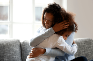 A mother and child share a comforting embrace while sitting on a couch, expressing deep emotional connection and support.
