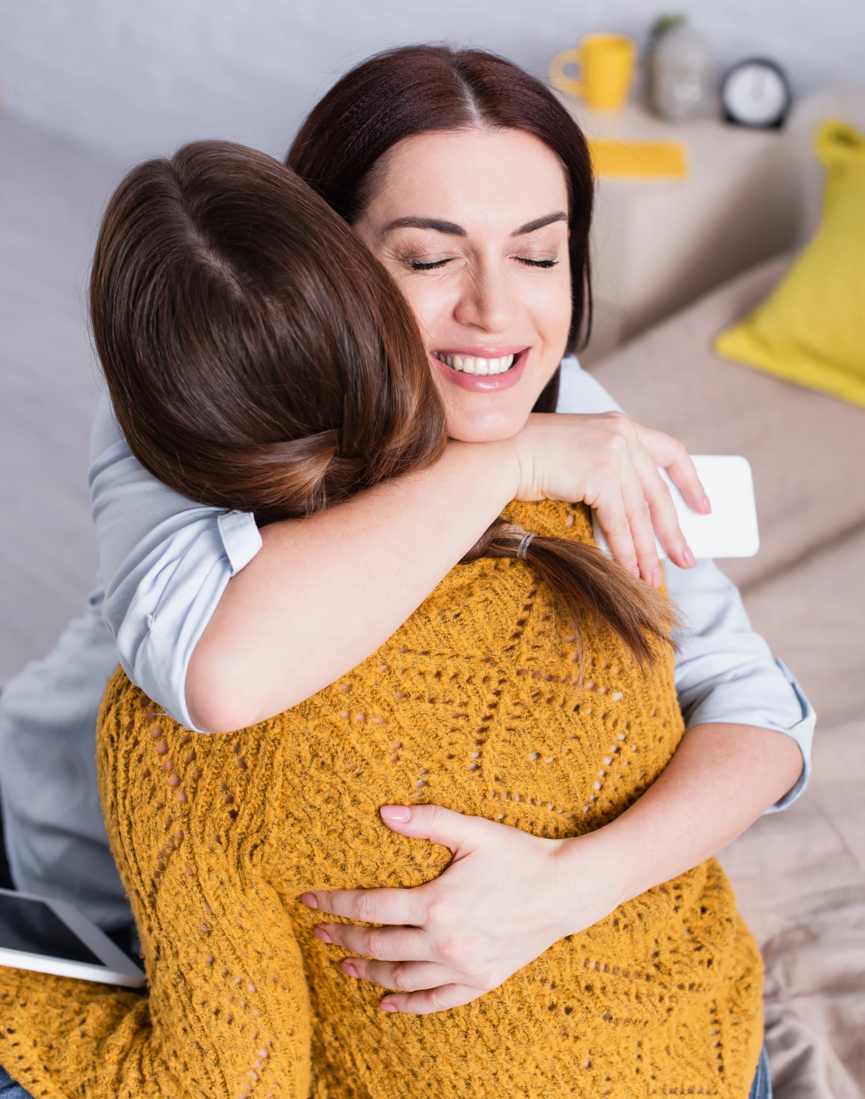 Warm embrace between two people on a couch—eyes closed, smiling—comfort and support in a safe home setting.