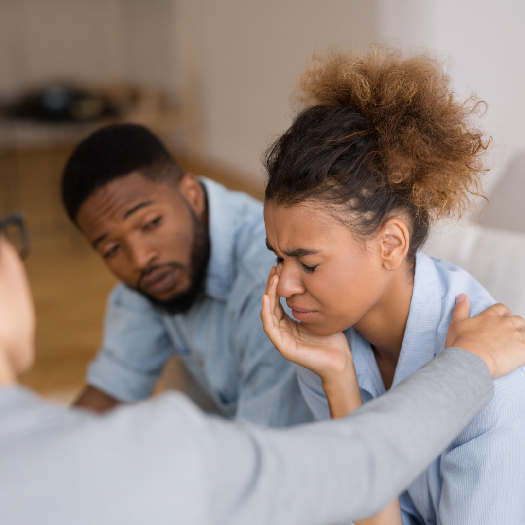 A parent coach and caregiver sit together at a table in a calm, focused setting, engaging in supportive dialogue while the coach offers a guiding hand and attentive expression.