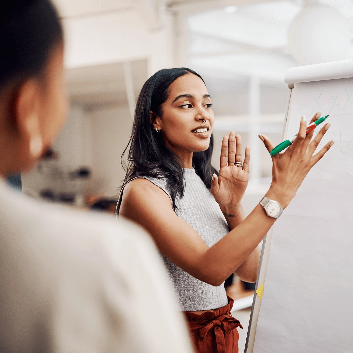 A professional woman stands beside a flip chart, using a green marker as she leads a training discussion with a small group.