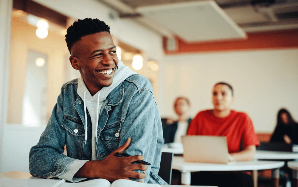 Smiling young adult sitting in a classroom, engaged in a trauma-informed training session with other students and professionals at ConnectionPlus Care.