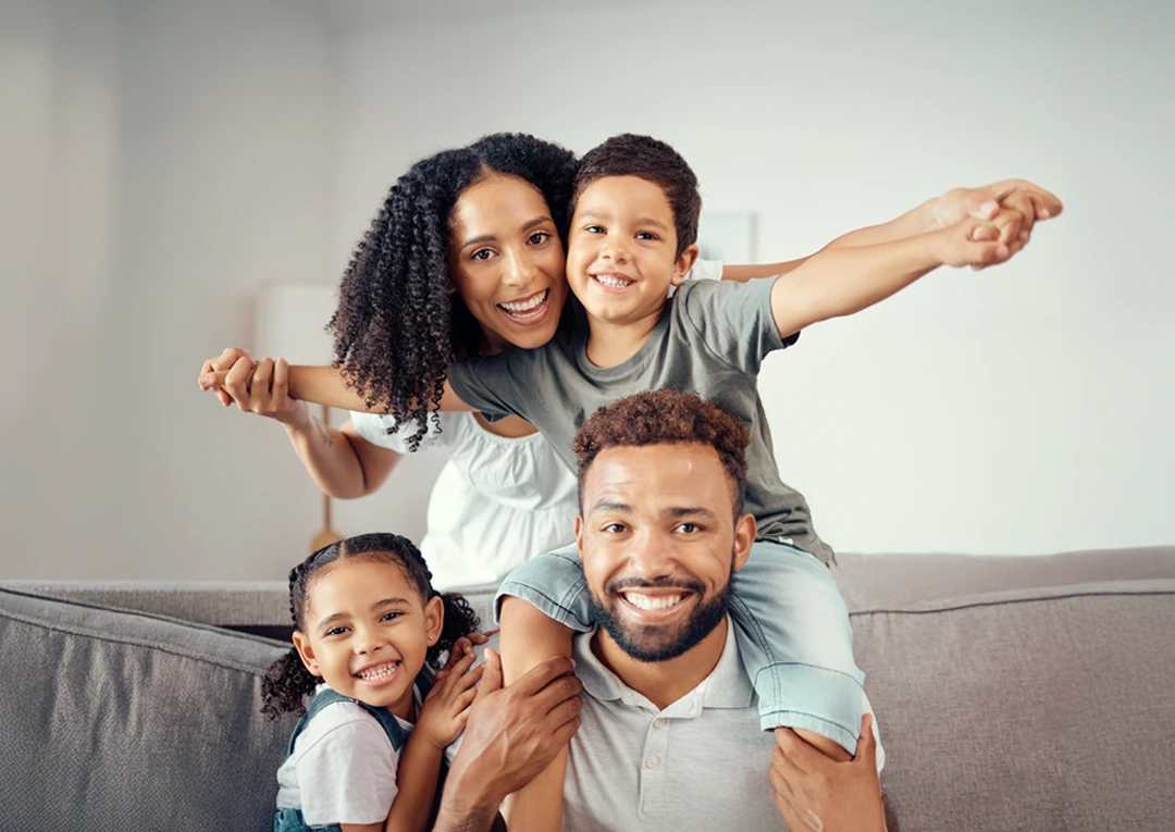 Foster family smiling together on the couch, parents embracing their children in a warm and happy moment.