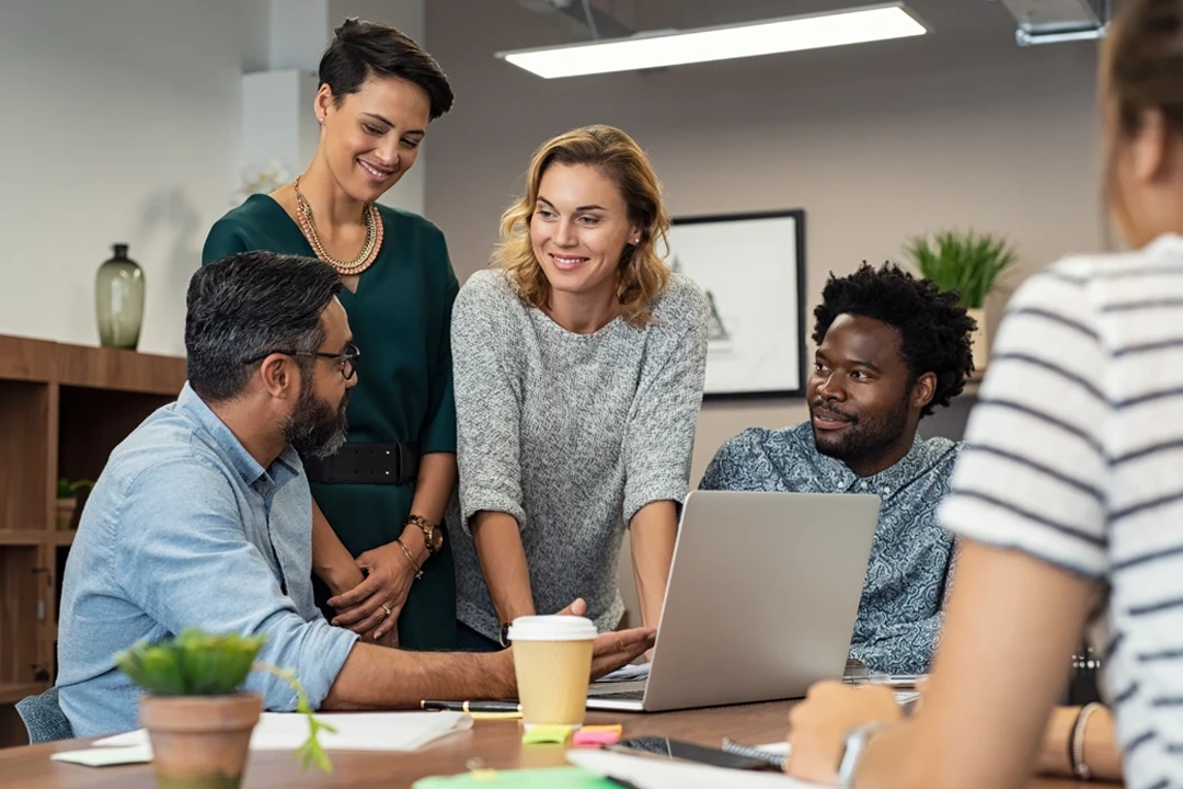 Team members collaborating during a professional meeting around a laptop in an office setting.
